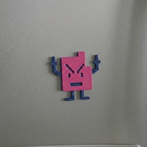 May include: A pink and blue magnet shaped like an angry pixelated character. The character has a square body, arms raised, and a frowning face. It is attached to a silver refrigerator door.
