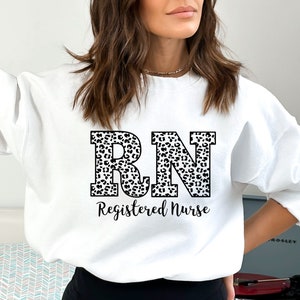 May include: White sweatshirt with a leopard print "RN Registered Nurse" design.