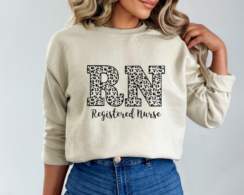 May include: A beige sweatshirt with a black and white leopard print "RN" design and the text "Registered Nurse" printed on the front.