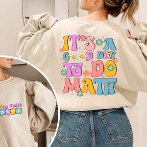 May include: A light beige sweatshirt with the text "It's a good day to do math" in colorful retro font with flowers and smiley faces.