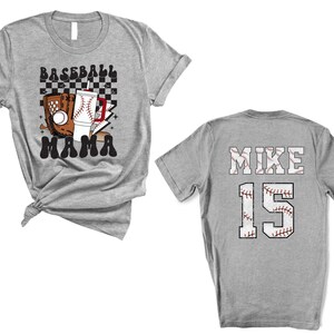 May include: A heather gray baseball t-shirt with the words "BASEBALL MAMA" and baseball-themed graphics on the front. The back of the shirt displays "MIKE" and the number "15" in a baseball stitch design.
