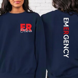 May include: Navy blue sweatshirt with the text "ER Olivia" in red on the front and "EMERGENCY" in white on the back.