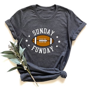 Pode incluir: Uma camiseta cinza escura com um gr&aacute;fico branco de uma bola de futebol e o texto "SUNDAY FUNDAY" em branco.