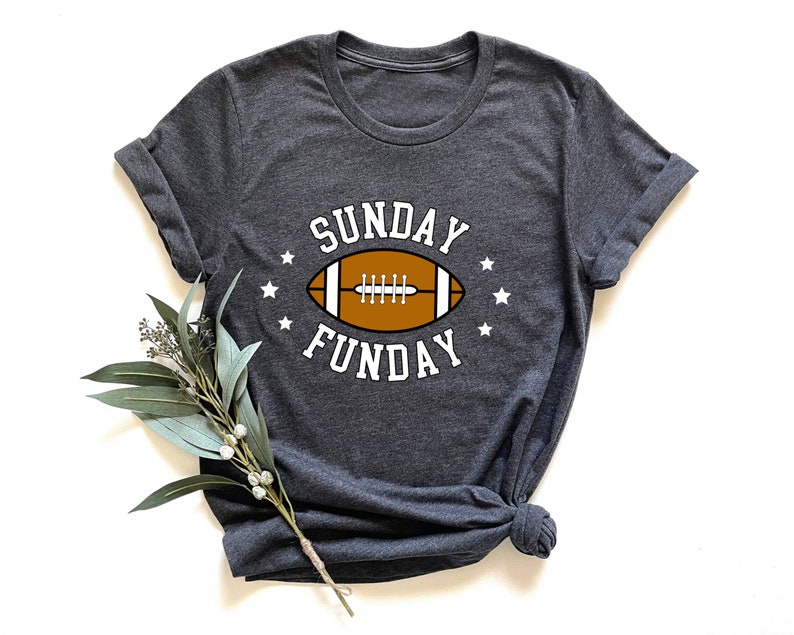 Pode incluir: Uma camiseta cinza escura com um gr&aacute;fico branco de uma bola de futebol e o texto "SUNDAY FUNDAY" em branco.