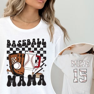 May include: White t-shirt with a baseball-themed graphic. The front features the words "BASEBALL MAMA" with a baseball, glove, and drink. The back displays "MIKE 15" in a baseball stitch design.