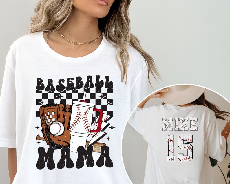 May include: White t-shirt with a baseball-themed graphic. The front features the words "BASEBALL MAMA" with a baseball, glove, and drink. The back displays "MIKE 15" in a baseball stitch design.