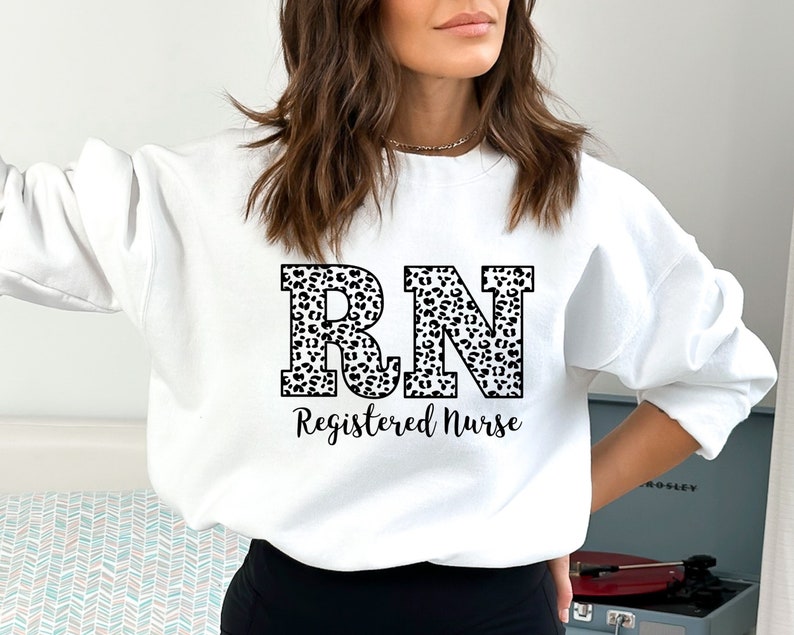 May include: White sweatshirt with a leopard print "RN Registered Nurse" design.