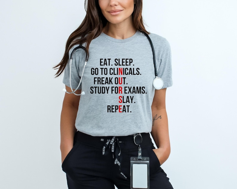 May include: A light gray t-shirt with the text "EAT. SLEEP. GO TO CLINICALS. FREAK OUT. STUDY FOR EXAMS. SLAY. REPEAT." in black and red lettering. A stethoscope hangs around the neck.