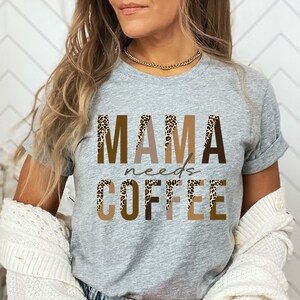 Op de afbeelding: Grijs T-shirt met de tekst "MAMA needs COFFEE" in bruine en beige letters met een luipaardprint.