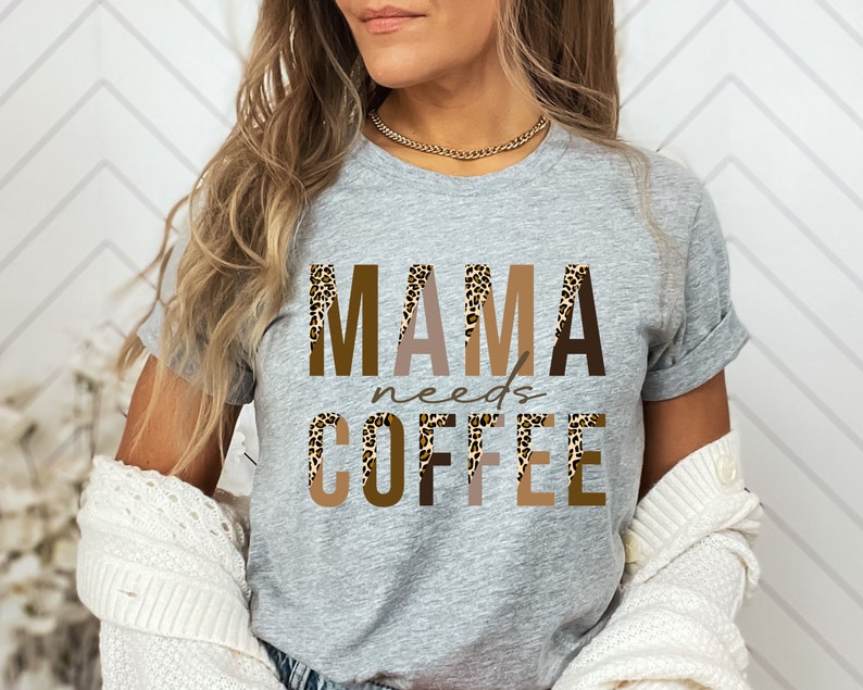 Op de afbeelding: Grijs T-shirt met de tekst "MAMA needs COFFEE" in bruine en beige letters met een luipaardprint.
