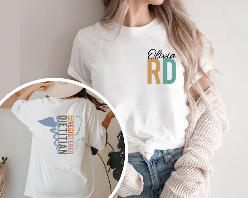 May include: White t-shirt with the text "Olivia RD" in black script and teal and gold block letters. The back of the shirt features a Registered Dietitian design with a caduceus and the words "Registered Dietitian" in teal and red.