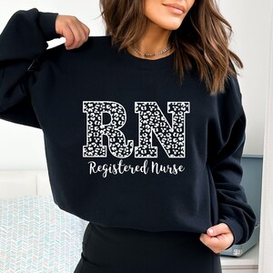 May include: Black sweatshirt with a white leopard print "RN" design and the text "Registered Nurse" below.