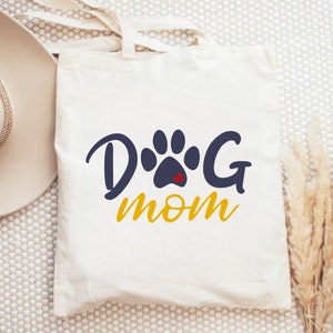 May include: White canvas tote bag with a blue paw print and the text "Dog Mom" in yellow.
