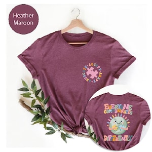 May include: Heather maroon t-shirt with a colorful puzzle piece design on the front and the text "Everyone Communicates Differently" with a cartoon earth holding a puzzle piece on the back.