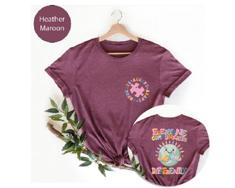 May include: Heather maroon t-shirt with a colorful puzzle piece design on the front and the text "Everyone Communicates Differently" with a cartoon earth holding a puzzle piece on the back.