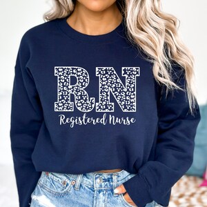 May include: A navy blue sweatshirt with a white leopard print "RN" design and the text "Registered Nurse" below.