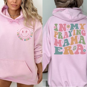 May include: Pink hoodie with a smiley face and the text "Praying Mama Era" on the front and the text "In My Praying Mama Era" on the back.