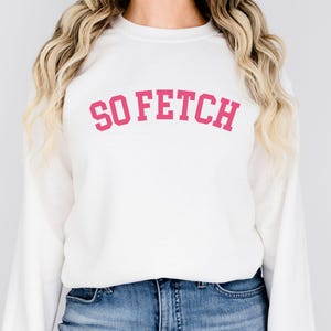 May include: White sweatshirt with long sleeves and a pink "SO FETCH" graphic printed on the front.