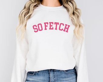Könnte beinhalten: Weißer Pullover mit langen Ärmeln und einem pinkfarbenen Aufdruck "SO FETCH" auf der Vorderseite.