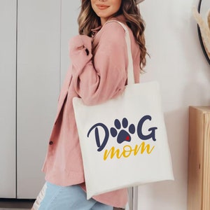 May include: A white tote bag with a blue paw print and the text "Dog Mom" in yellow letters.