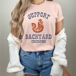 May include: A pink t-shirt with a distressed graphic of a rooster and the text "Support Backyard Chickens".