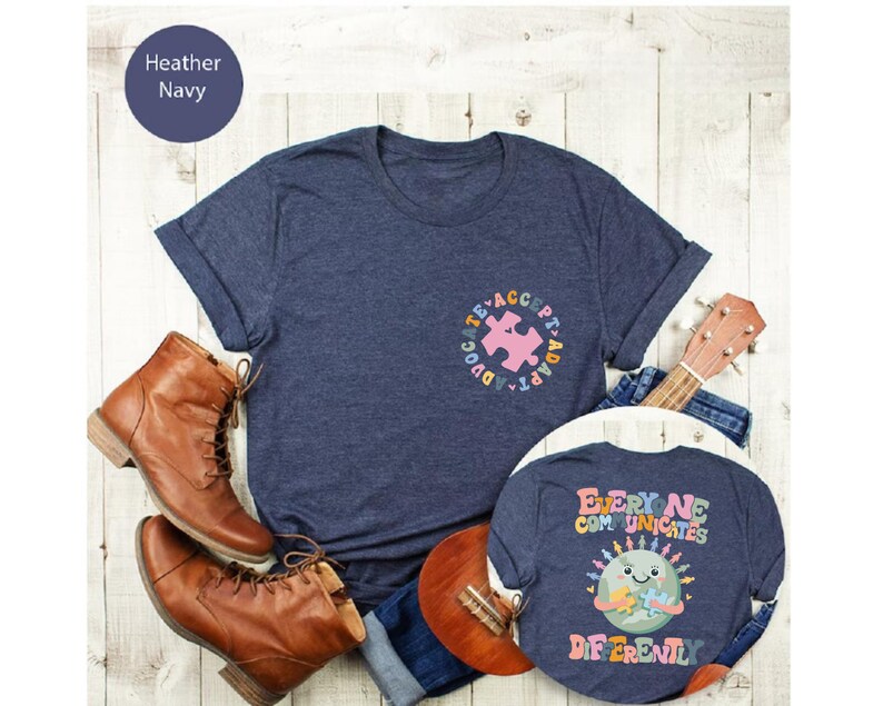 May include: Two navy blue t-shirts with autism awareness designs. The larger shirt has a puzzle piece with the words "Advocate, Accept, Adapt" around it. The smaller shirt has a cartoon earth with the words "Everyone Communicates Differently".