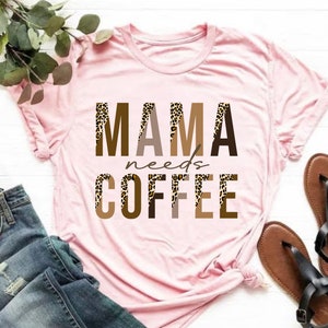 Op de afbeelding: Roze T-shirt met de tekst "MAMA needs COFFEE" in bruine letters met een luipaardprint.