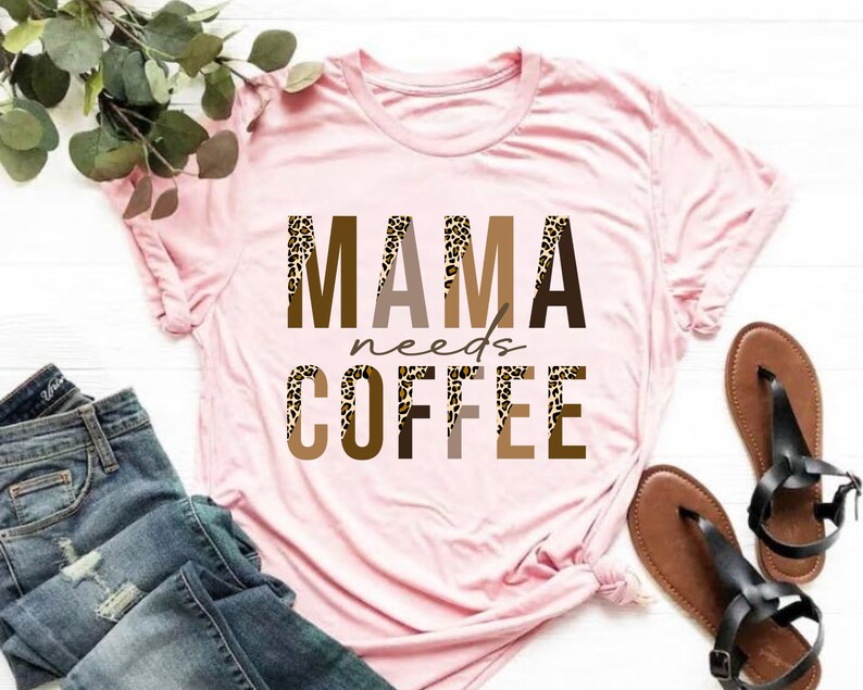 Op de afbeelding: Roze T-shirt met de tekst "MAMA needs COFFEE" in bruine letters met een luipaardprint.