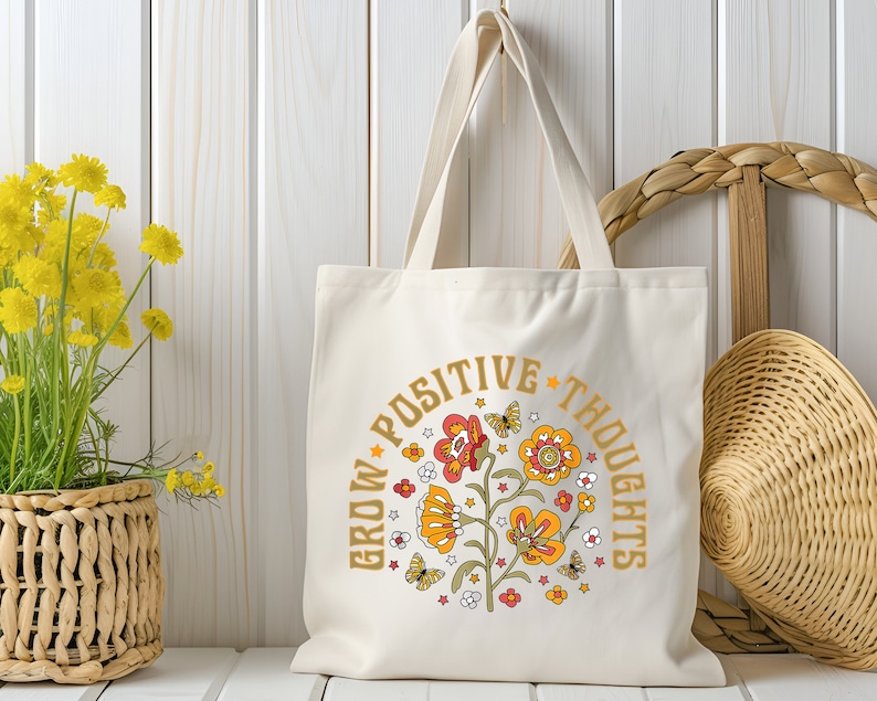 May include: A white canvas tote bag with a floral design and the text "Grow Positive Thoughts" in gold lettering.