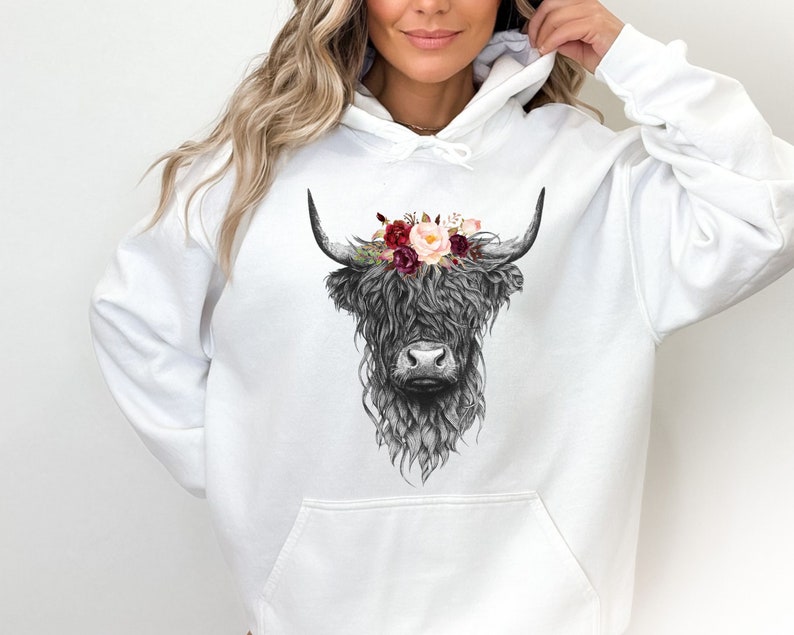 Puede incluir: Sudadera blanca con una ilustraci&oacute;n en blanco y negro de una vaca de las tierras altas con una corona de flores. Las flores son rojas, rosas y blancas.