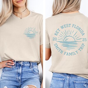 May include: A tan t-shirt with a blue graphic of a sunset over the ocean with birds flying. The back of the shirt has a blue graphic of a sunset with the text "Key West Florida 2025 Smith Family Trip".