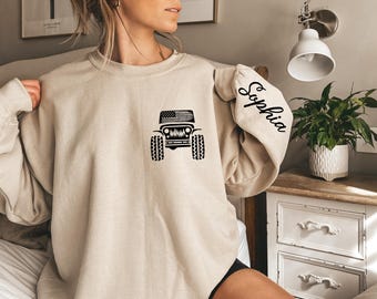 May include: A beige sweatshirt with a black Jeep silhouette and an American flag on the front. The left sleeve has the name "Sophia" written in black.