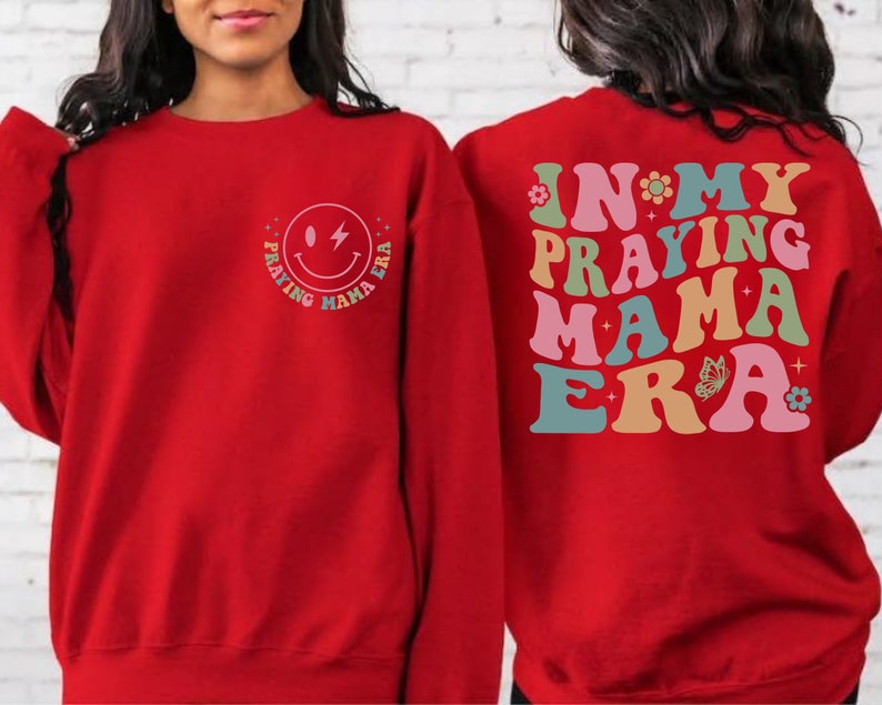 May include: Red sweatshirt with a smiley face graphic that says "Praying Mama Era" on the front and "In My Praying Mama Era" on the back.