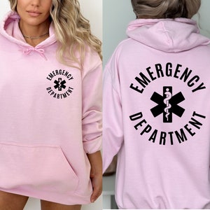 May include: Pink hoodie with a black graphic of a medical symbol and the text "Emergency Department".