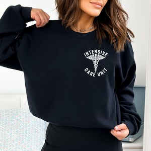 May include: Black crewneck sweatshirt with the text "INTENSIVE CARE UNIT" and a medical caduceus symbol in white. The sweatshirt is a solid black color.