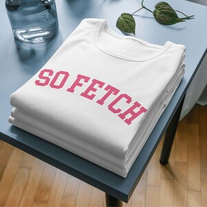 Op de afbeelding: Een wit T-shirt met de tekst "SO FETCH" in roze letters.