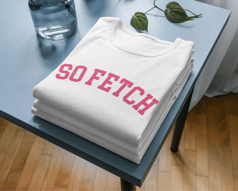 Op de afbeelding: Een wit T-shirt met de tekst "SO FETCH" in roze letters.