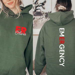 May include: A green hooded sweatshirt with the text "ER Olivia" in red on the front and "EMERGENCY" in white on the back.