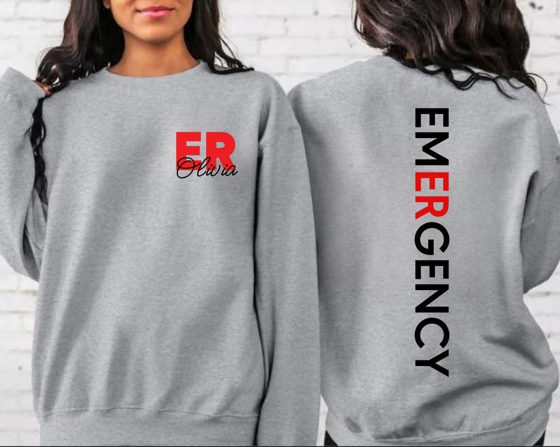 May include: Gray sweatshirt with the text "ER Olivia" in red and black on the front and "EMERGENCY" in black on the back.