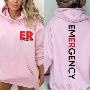 May include: Pink hoodie with the text "ER Olivia" on the front and "EMERGENCY" vertically down the back.