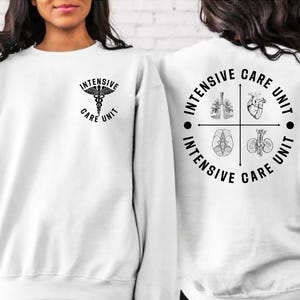 May include: White sweatshirt with black text and graphics. The front features a medical symbol and the words "Intensive Care Unit." The back displays a circular design with the words "Intensive Care Unit" and illustrations of internal organs.