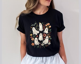 May include: A black short-sleeve t-shirt featuring a central graphic print of five white ghosts, one wearing a small gold crown, surrounded by colorful orange, pink, and yellow flowers, green leaves, and a small grey bat against a dark background.