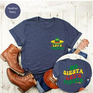 May include: Two navy blue t-shirts with a fiesta theme. The larger shirt has a green, red, and yellow sombrero with the text "Let's Fiesta". The smaller shirt has the text "No Siesta Let's Fiesta".