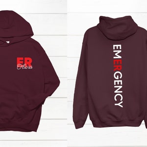 May include: Burgundy hoodie with a white and red "EMERGENCY" graphic on the back and a red "ER" graphic with the name "Olivia" on the front.