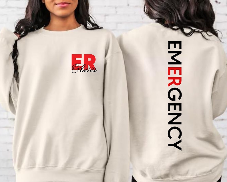 May include: A cream-colored sweatshirt with the text "ER Olivia" in red and black on the front and "EMERGENCY" in black on the back.