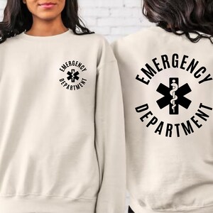 May include: A cream colored sweatshirt with the text "EMERGENCY DEPARTMENT" and a medical symbol on the back. The same text and symbol are on the front of the sweatshirt in a smaller size.