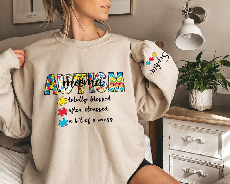 May include: A beige sweatshirt with the text "Autism mama totally blessed often stressed a bit of a mess" and a puzzle piece design. The left sleeve has the text "My kids" with a puzzle piece design.