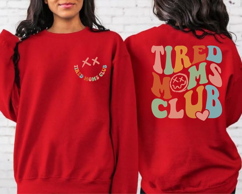 Puede incluir: Sudadera roja con el texto "Tired Moms Club" en colores arco&iacute;ris en la espalda y una peque&ntilde;a carita sonriente con una "X" por ojos en la parte delantera.