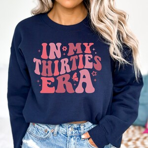 May include: A navy blue sweatshirt with a pink and red graphic that says "In My Thirties Era" with stars and a butterfly.