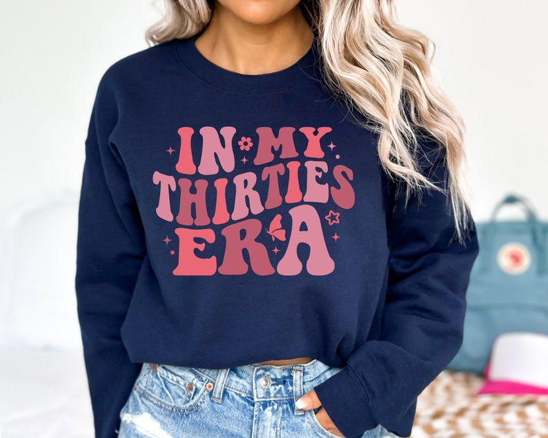 May include: A navy blue sweatshirt with a pink and red graphic that says "In My Thirties Era" with stars and a butterfly.